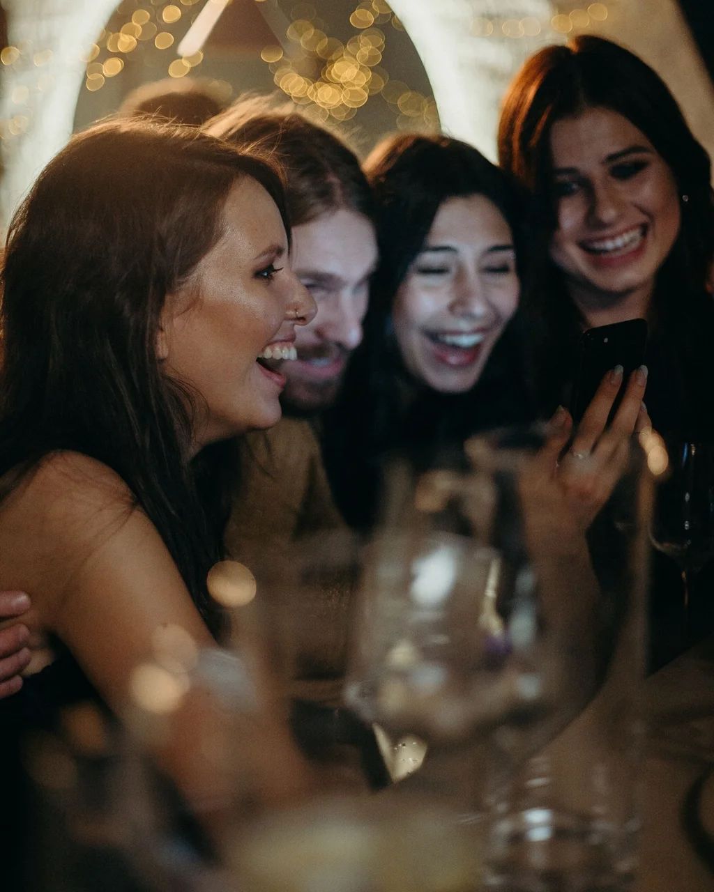 Before: four friends laughing at a phone in a bar