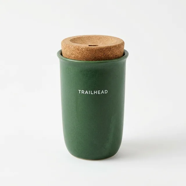 Reference photo of a green ceramic travel mug with a cork lid and the logo TRAILHEAD